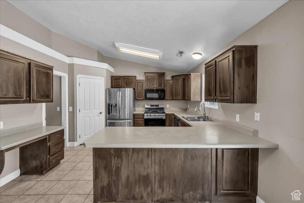 Kitchen featuring stainless steel appliances, vaulted ceiling, dark brown cabinets, light countertops, and light tile patterned flooring