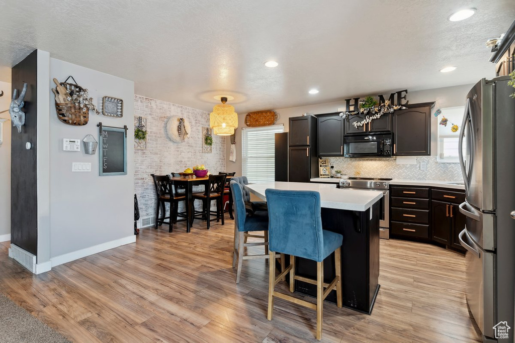 Kitchen with stainless steel appliances, a center island, light countertops, a breakfast bar area, and healthy amount of natural light