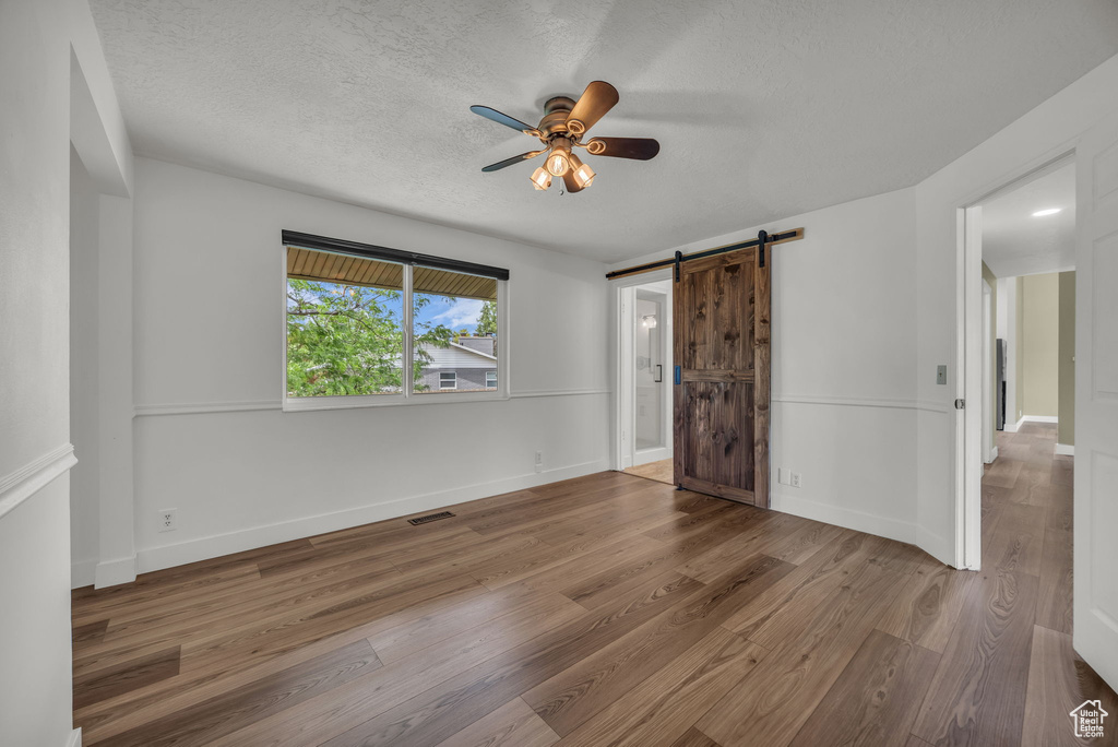 Unfurnished bedroom with a barn door, wood finished floors, a textured ceiling, and ceiling fan