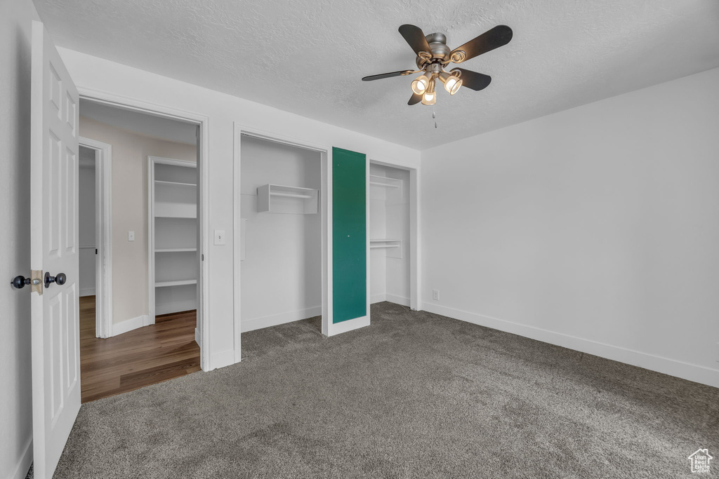 Unfurnished bedroom with carpet, a textured ceiling, two closets, and ceiling fan