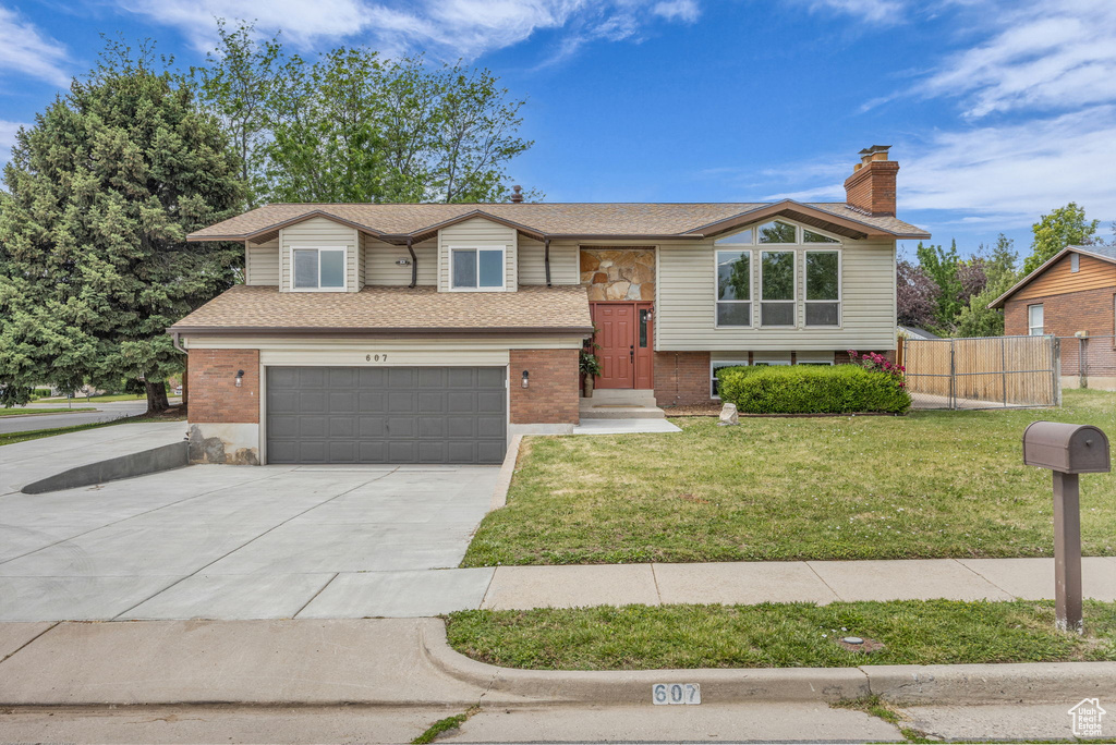 Split foyer home with driveway, an attached garage, brick siding, roof with shingles, and a chimney