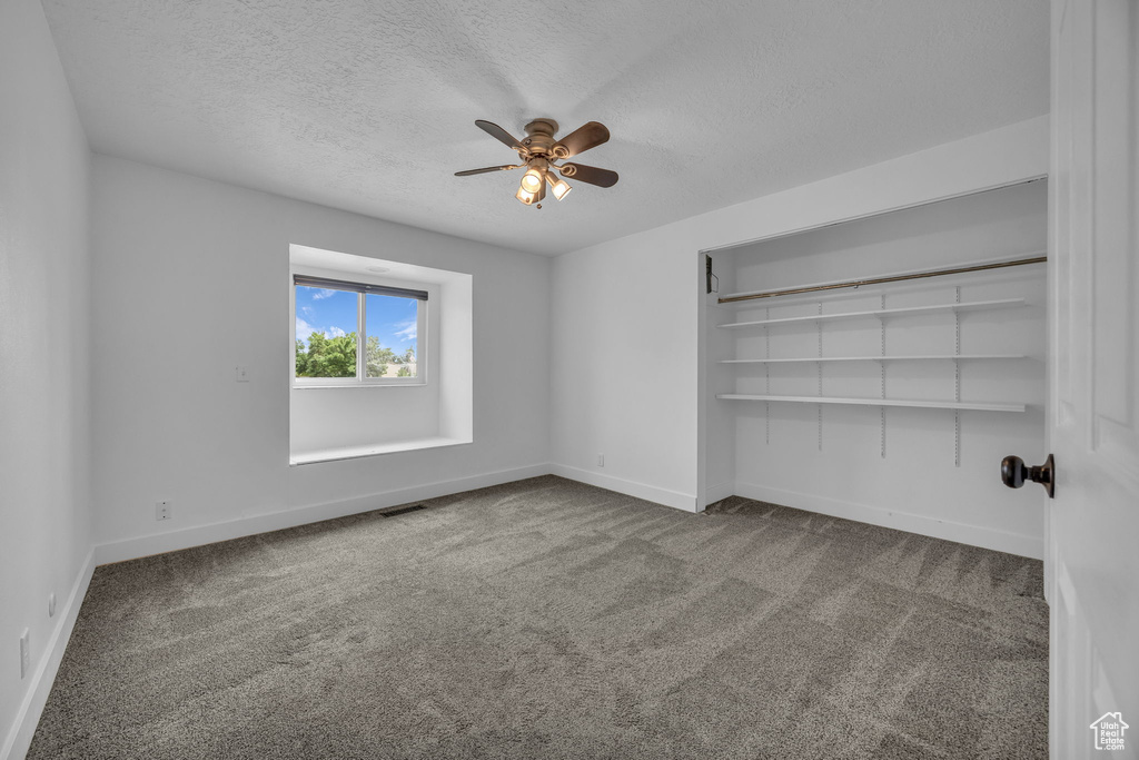 Carpeted empty room featuring a textured ceiling and a ceiling fan