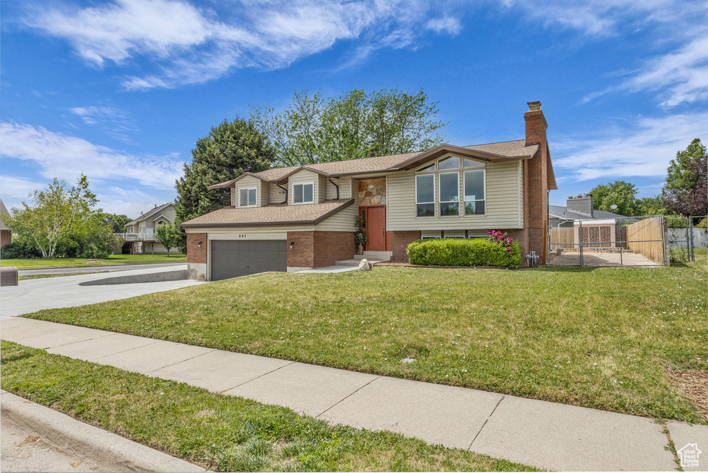 Split foyer home with brick siding, concrete driveway, a chimney, a shingled roof, and a garage