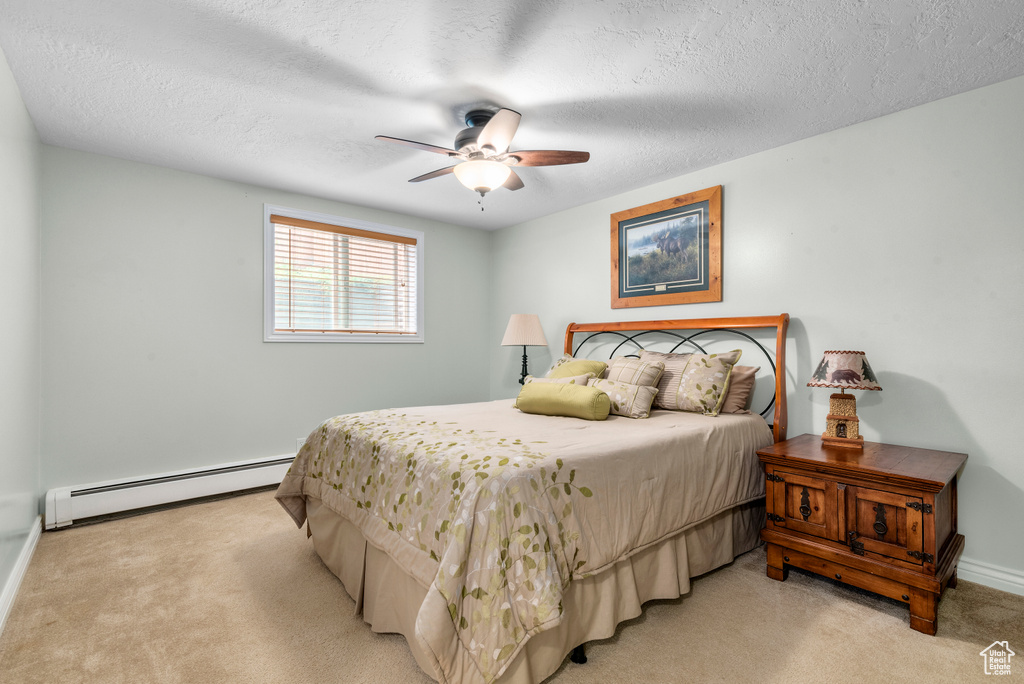 Bedroom featuring baseboard heating, light colored carpet, a textured ceiling, and a ceiling fan