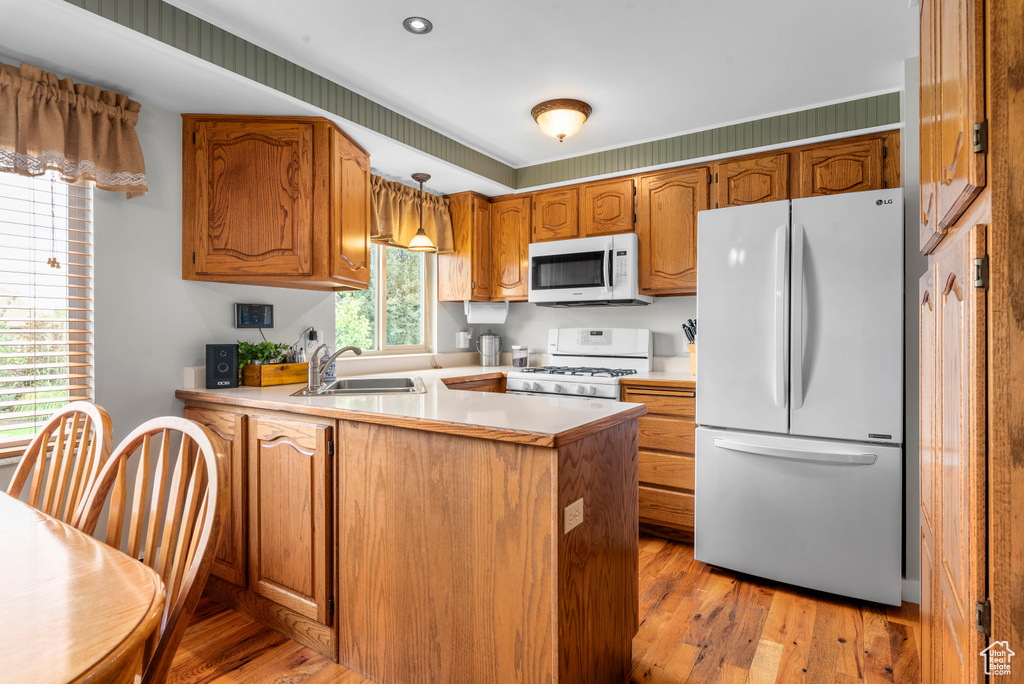 Kitchen featuring white appliances, a peninsula, light countertops, light wood-type flooring, and brown cabinets