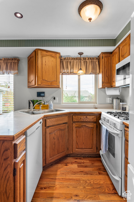 Kitchen with white appliances, a peninsula, wood finished floors, plenty of natural light, and recessed lighting