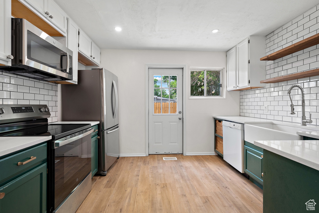 Kitchen with green cabinetry, stainless steel appliances, light countertops, open shelves, and recessed lighting