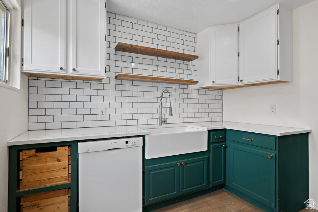 Kitchen featuring white dishwasher, backsplash, white cabinetry, light countertops, and light wood-style flooring