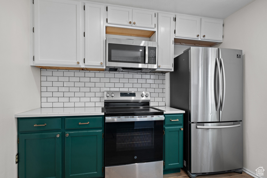 Kitchen with stainless steel appliances, light countertops, green cabinets, and decorative backsplash