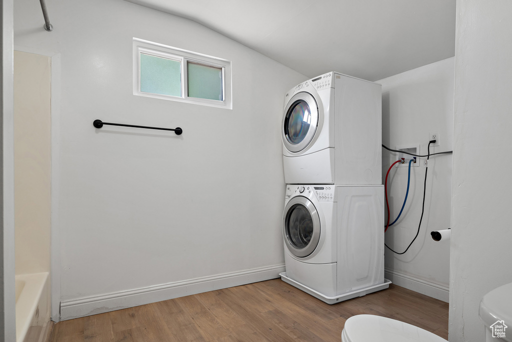 Washroom with stacked washing machine and dryer and wood finished floors