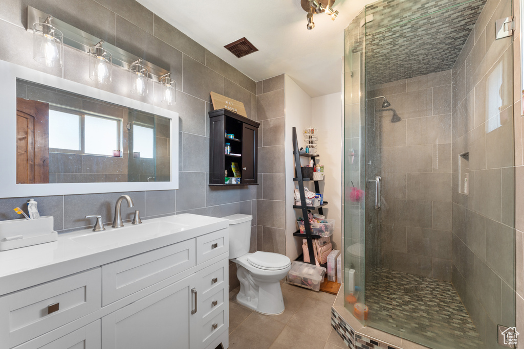 Full bath featuring tile walls, toilet, vanity, tiled shower, and tile patterned flooring