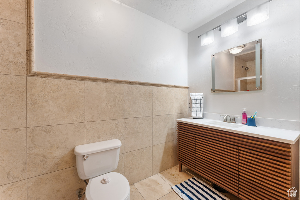Bathroom with toilet, vanity, tile walls, tile patterned flooring, and wainscoting