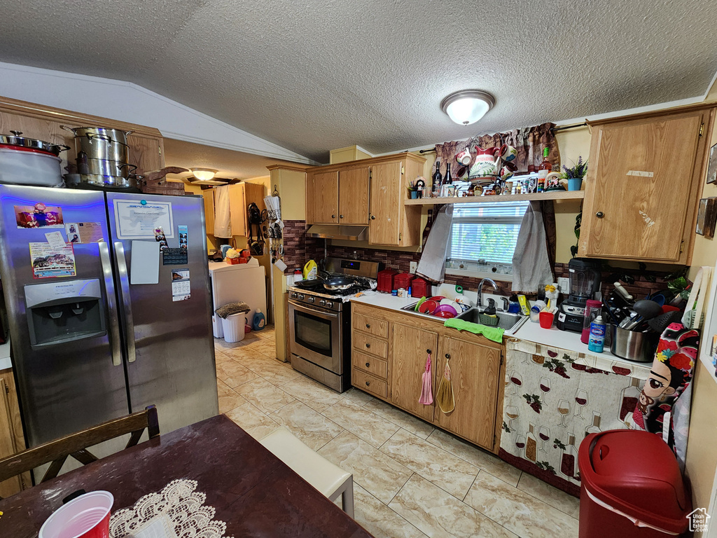 Kitchen with stainless steel appliances, vaulted ceiling, under cabinet range hood, a textured ceiling, and open shelves