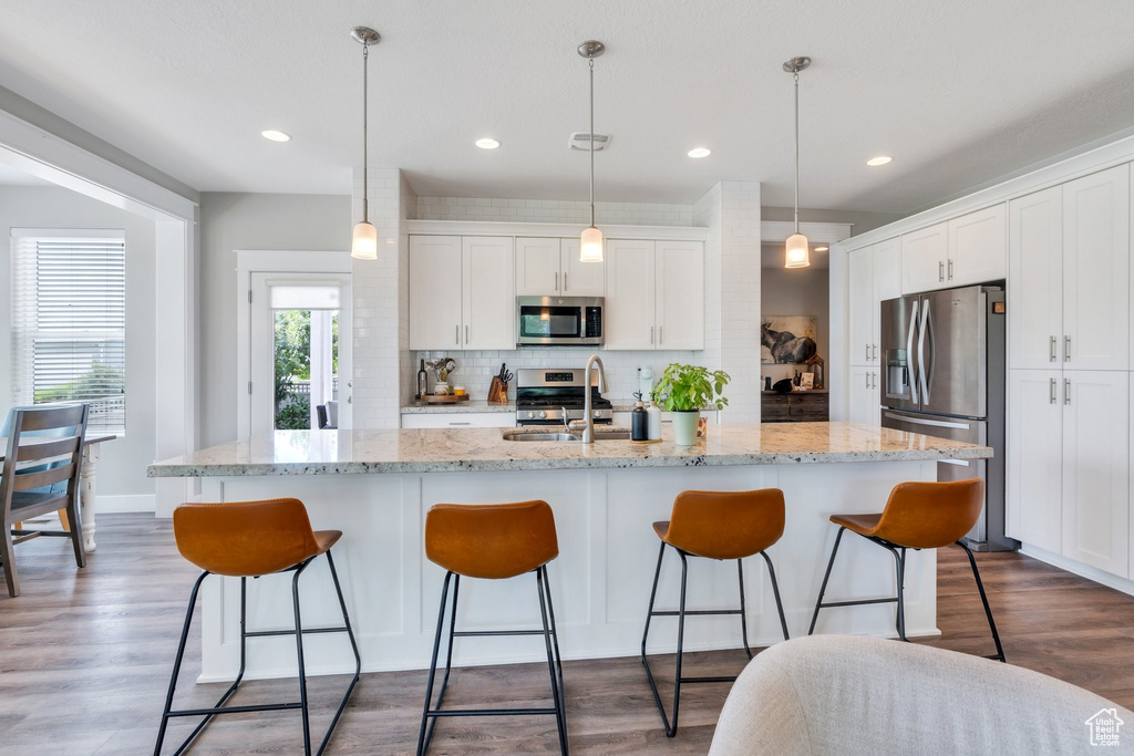 Kitchen featuring stainless steel appliances, backsplash, white cabinetry, a kitchen breakfast bar, and recessed lighting