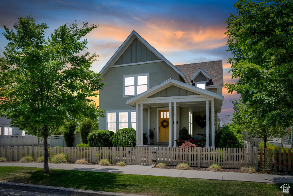 View of front of house with covered porch, board and batten siding, a shingled roof, a gate, and a fenced front yard