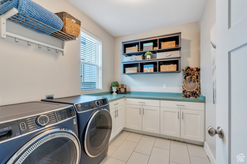 Washroom featuring washer and dryer, cabinet space, and light tile patterned flooring