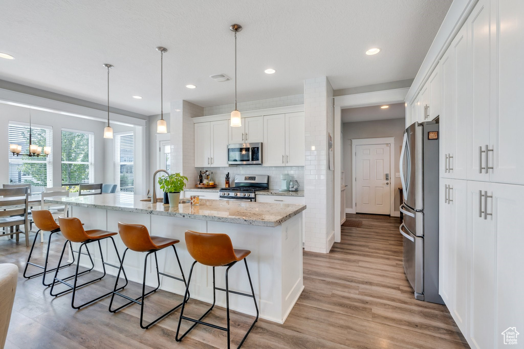 Kitchen featuring stainless steel appliances, white cabinetry, a kitchen bar, light wood-style flooring, and recessed lighting