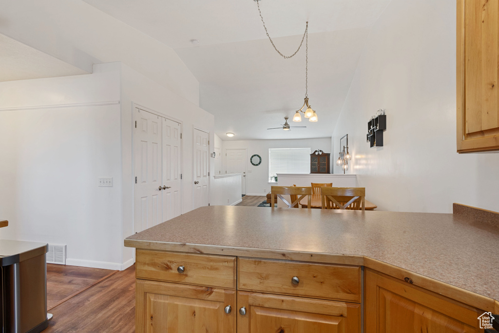 Kitchen featuring vaulted ceiling, a peninsula, dark wood finished floors, ceiling fan, and decorative light fixtures