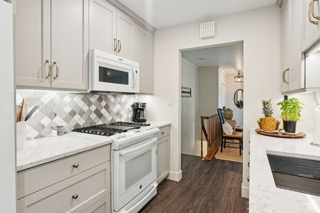 Kitchen with white appliances, dark wood-style floors, tasteful backsplash, light stone countertops, and white cabinets