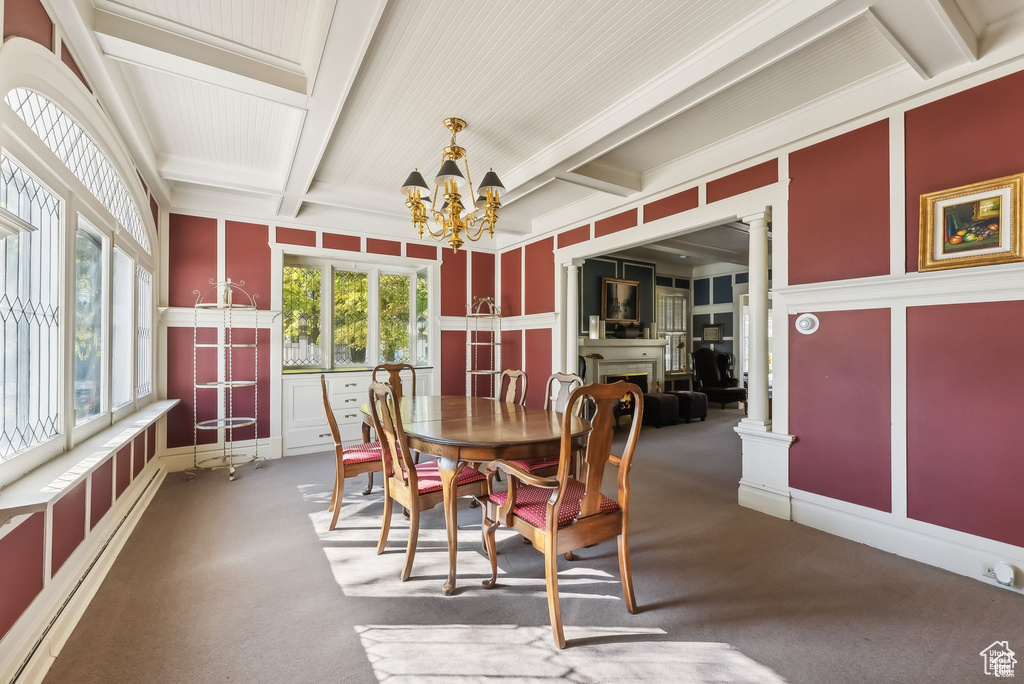 Carpeted dining area featuring a decorative wall, a chandelier, plenty of natural light, beam ceiling, and decorative columns