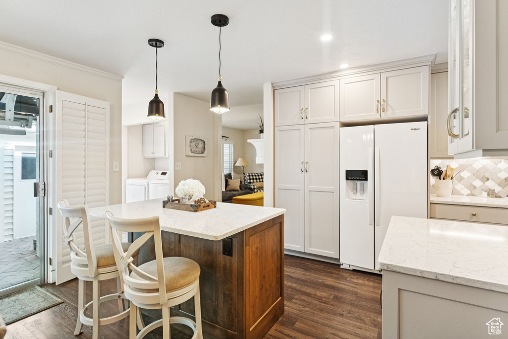 Kitchen featuring white refrigerator with ice dispenser, independent washer and dryer, dark wood-style flooring, decorative light fixtures, and ornamental molding