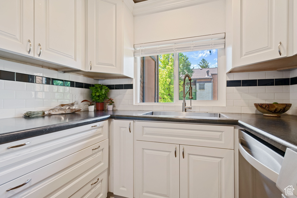 Kitchen featuring stainless steel dishwasher, white cabinetry, decorative backsplash, and dark countertops