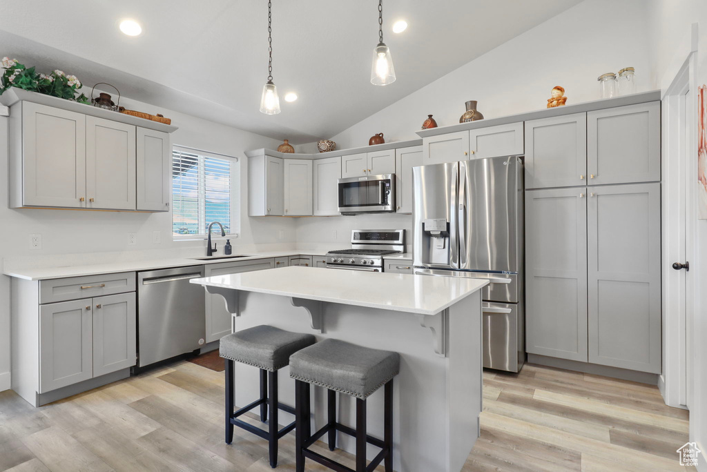 Kitchen featuring appliances with stainless steel finishes, vaulted ceiling, a kitchen breakfast bar, light countertops, and a kitchen island