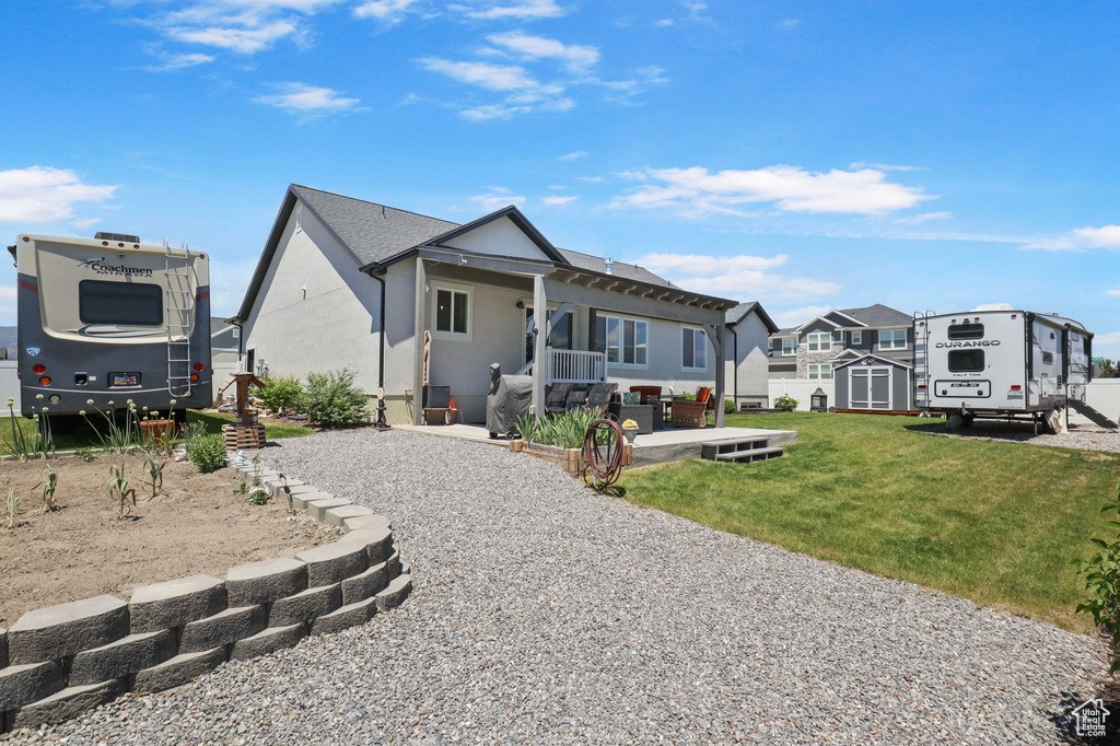 View of front of house with a storage shed, stucco siding, a front yard, and a patio