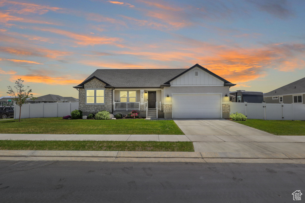 View of front of property featuring an attached garage, stone siding, concrete driveway, covered porch, and a gate