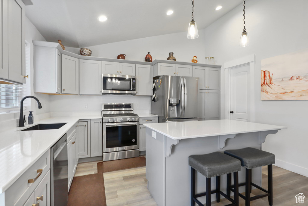 Kitchen with stainless steel appliances, a breakfast bar area, a center island, light wood-style floors, and light countertops