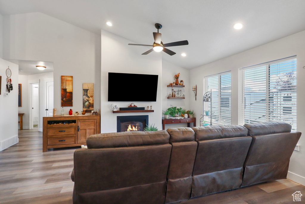 Living area with lofted ceiling, ceiling fan, a glass covered fireplace, light wood-style flooring, and recessed lighting