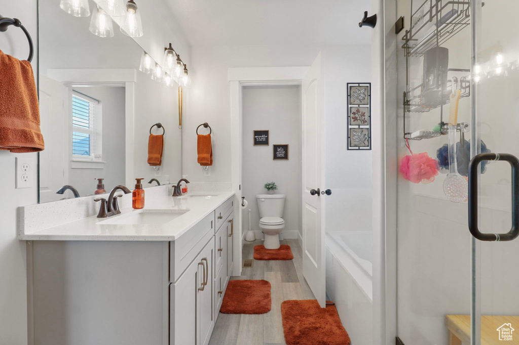 Full bathroom with double vanity, wood finished floors, a shower with shower door, and a tub to relax in