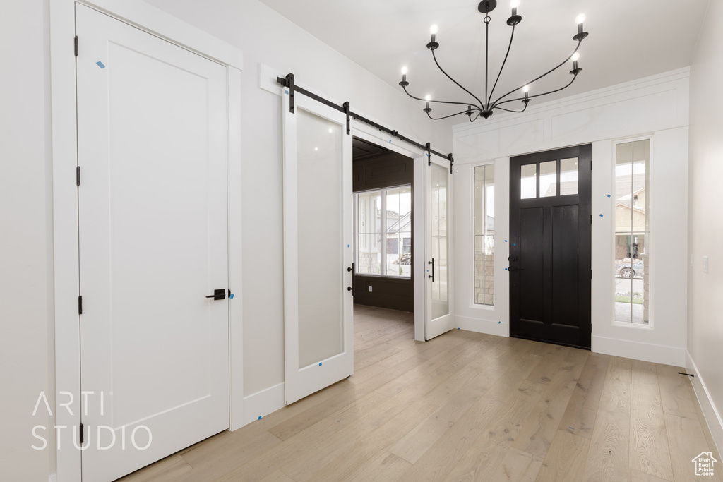 Foyer entrance with baseboards, a barn door, light wood finished floors, and a chandelier