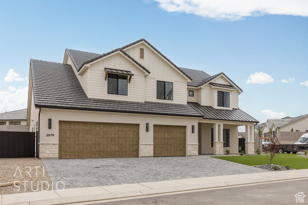View of front of home with stone siding, a garage, a standing seam roof, and decorative driveway