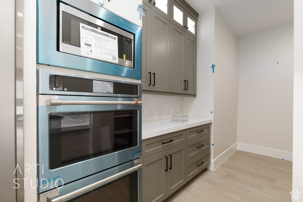 Kitchen featuring stainless steel appliances, baseboards, backsplash, light wood-style flooring, and gray cabinets