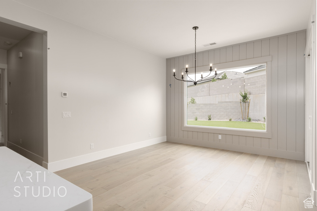 Unfurnished dining area with wood finished floors, a chandelier, and baseboards