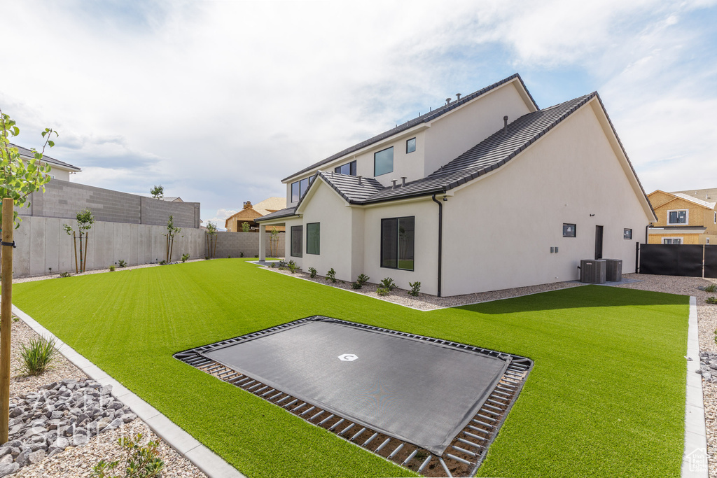 Rear view of house with a fenced backyard, stucco siding, and a trampoline
