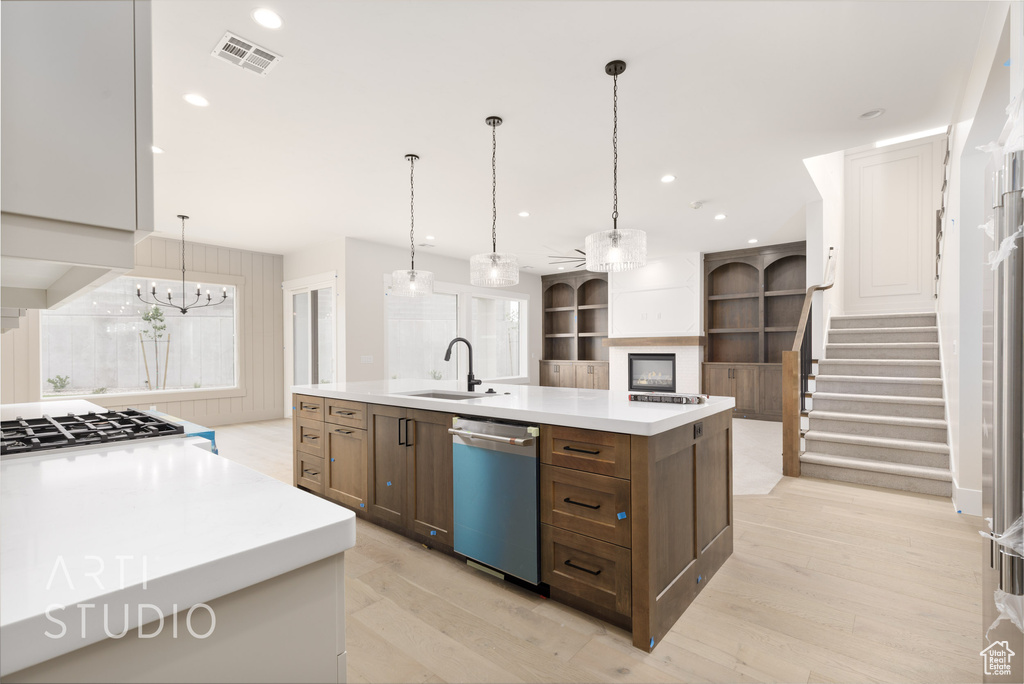 Kitchen with dishwashing machine, a sink, light countertops, a large island with sink, and light wood-type flooring