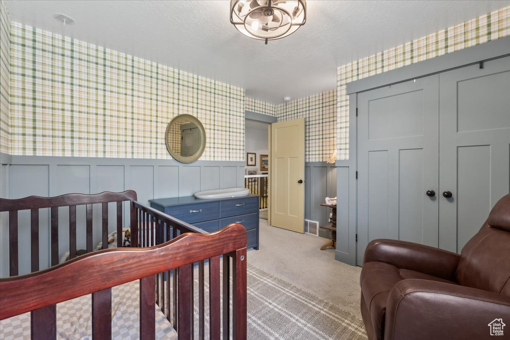 Bedroom featuring wallpapered walls, light carpet, a closet, wainscoting, and a decorative wall