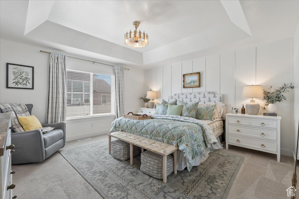 Carpeted bedroom featuring a raised ceiling and a chandelier