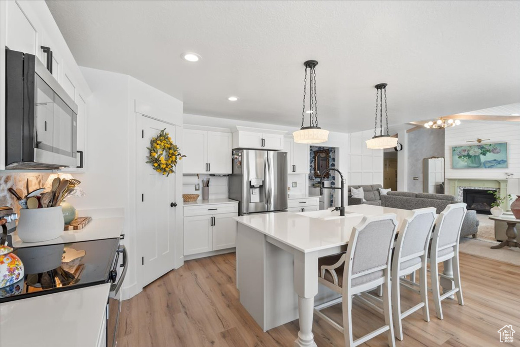 Kitchen with stainless steel appliances, a kitchen bar, light wood-style floors, white cabinets, and recessed lighting