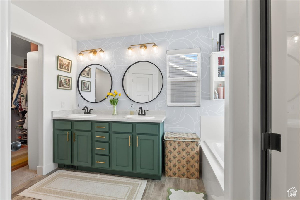 Full bathroom featuring double vanity, wood finished floors, a garden tub, wallpapered walls, and a spacious closet