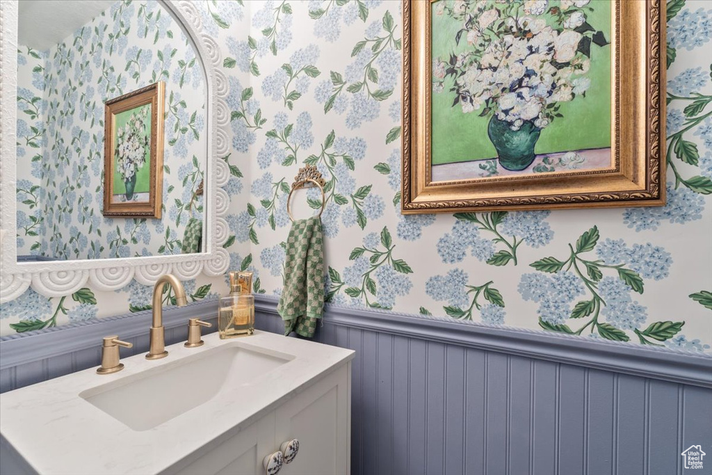 Bathroom with wallpapered walls, wainscoting, and vanity
