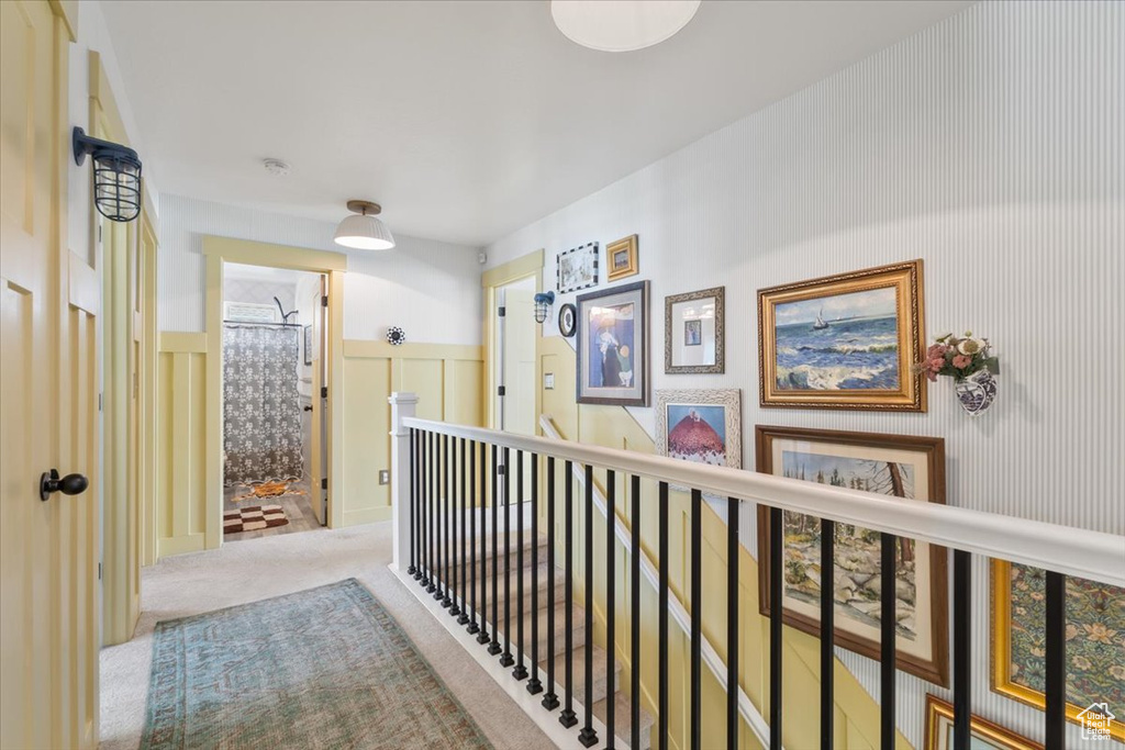 Corridor featuring wainscoting, carpet flooring, a decorative wall, and an upstairs landing