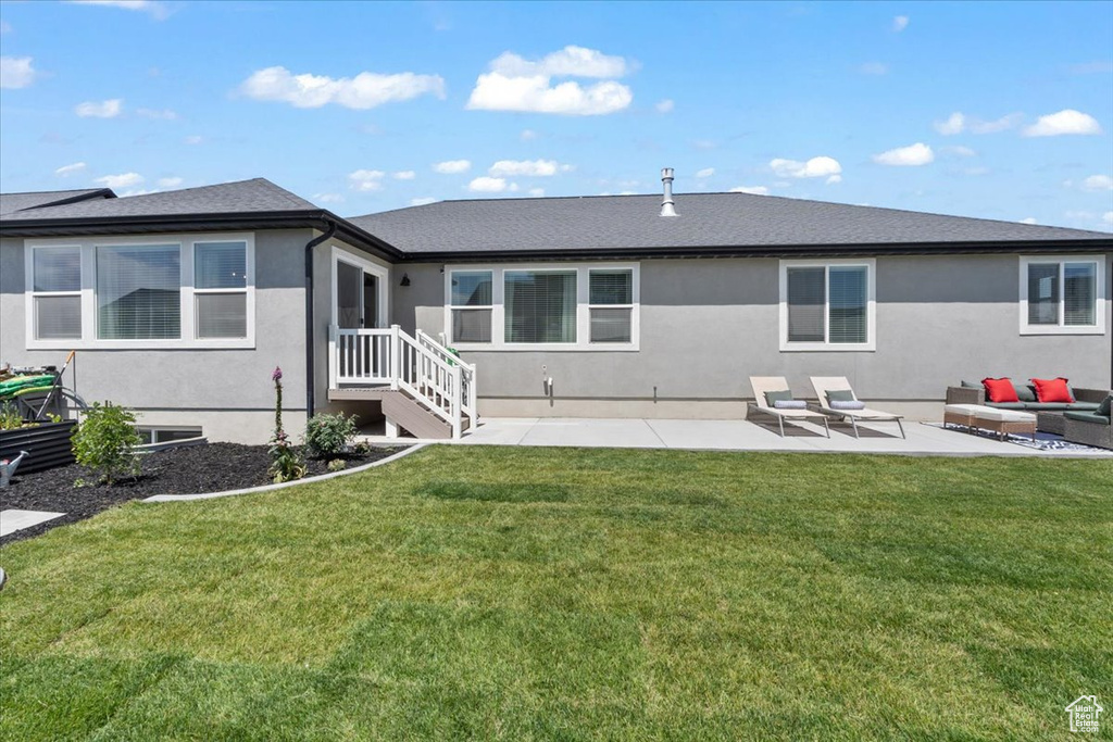 Back of house with stucco siding, a patio area, an outdoor living space, and a lawn