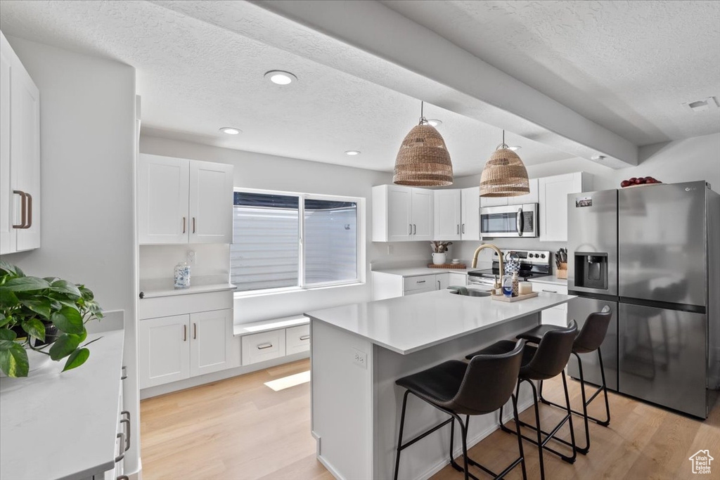 Kitchen featuring appliances with stainless steel finishes, a textured ceiling, light wood-style floors, white cabinetry, and light countertops
