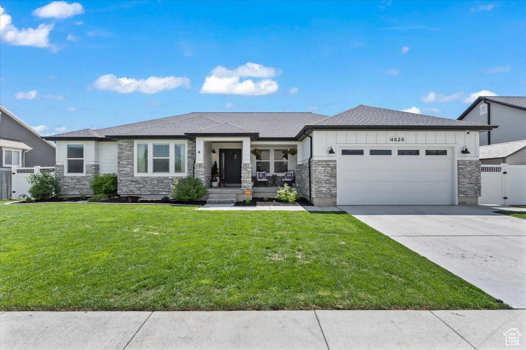 Prairie-style home with stone siding, a garage, driveway, covered porch, and a gate