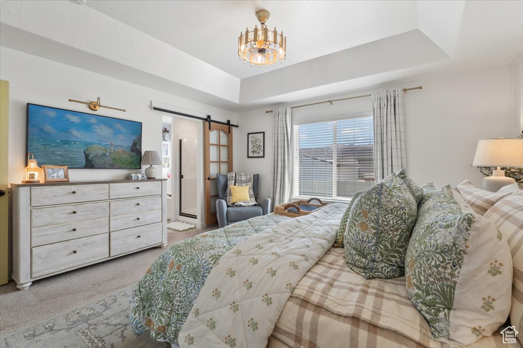 Carpeted bedroom featuring a barn door, a tray ceiling, and a chandelier
