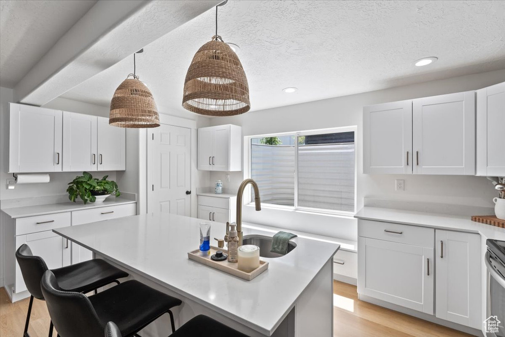 Kitchen featuring light countertops, light wood-style floors, white cabinetry, a breakfast bar area, and a textured ceiling