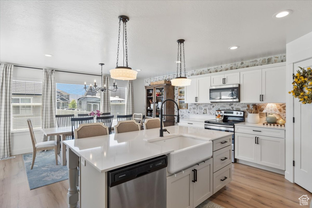 Kitchen featuring stainless steel appliances, tasteful backsplash, hanging light fixtures, light wood-style floors, and recessed lighting